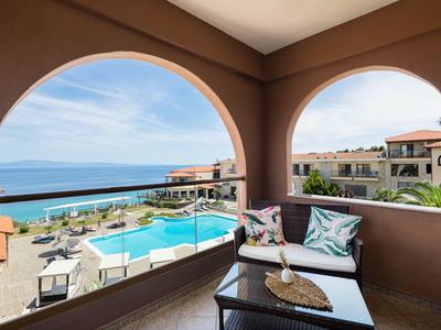 Balkon s posezením s výhledem na bazén a moře pod modrou oblohou.