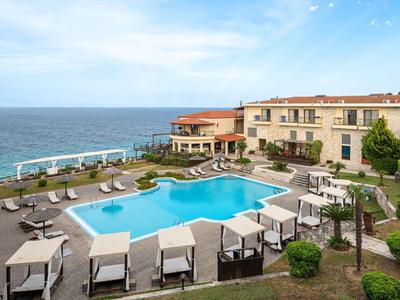 Hôtel avec piscine et chaises longues surplombant la mer et le ciel bleu.