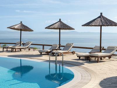 Bazénová část s lehátky a slaměnými slunečníky s výhledem na moře za jasné oblohy.