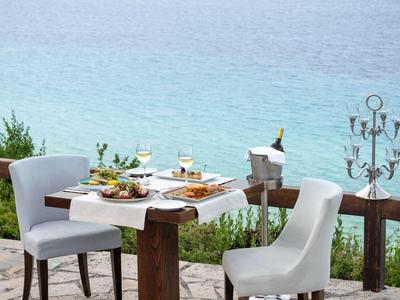 Un espace repas en plein air avec deux chaises blanches et une table dressée avec vue sur la mer.
