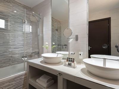 Moderní koupelna s bílou keramikou, dveřmi do sprchového koutu a velkými zrcadly.