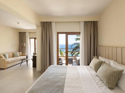 Světle zařízený hotelový pokoj s postelí, pohovkou a výhledem na moře z terasy.