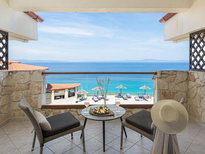 Balcon avec table, chaises et vue sur la piscine et la mer sous un ciel dégagé.