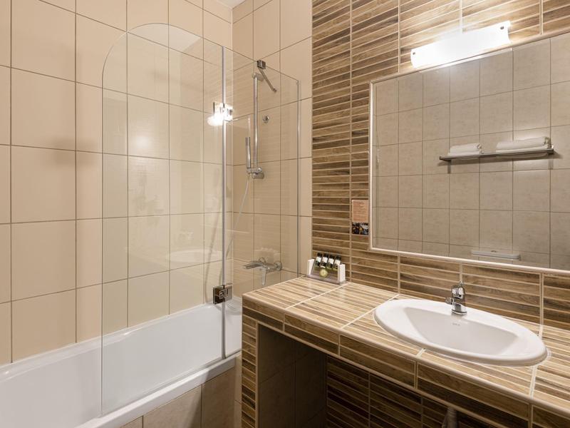 Moderní koupelna s vanou, umyvadlem a velkým zrcadlem v teplých hnědých a béžových tónech.