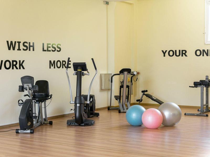 Malá posilovna s kardio přístroji a gymnastickými míči před zdí s motivačním nápisem.