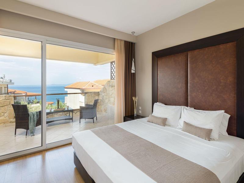 Světý hotelový pokoj s manželskou postelí a terasou s výhledem na moře.