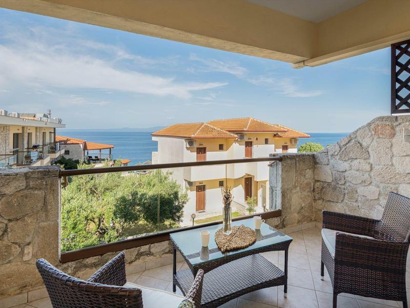 Balkon se dvěma židlemi, stolem a výhledem na moře v rekreačním areálu.