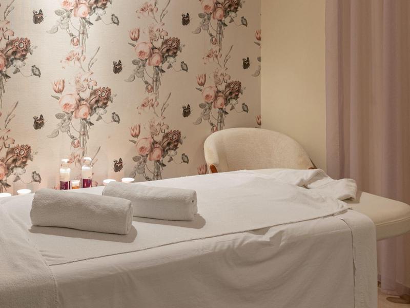 Prostorná masážní místnost s květinovou tapetou, masážním stolem a bílými ručníky.
