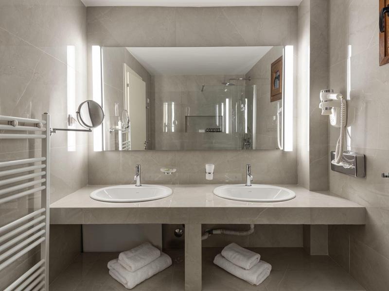 Moderní koupelna s dvojitými umyvadly, velkými zrcadly a sušáky na ručníky.