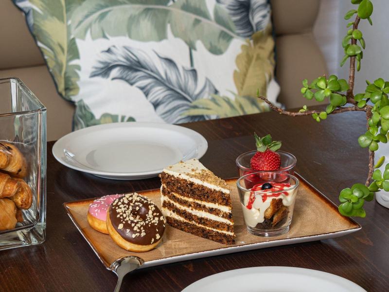 Kávový stolek s dortem, pečivem, dvěma talíři a dekorativními polštáři v pozadí.