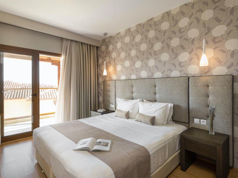 Moderní hotelový pokoj s manželskou postelí, květinovou tapetou a balkonovým oknem se závěsy.