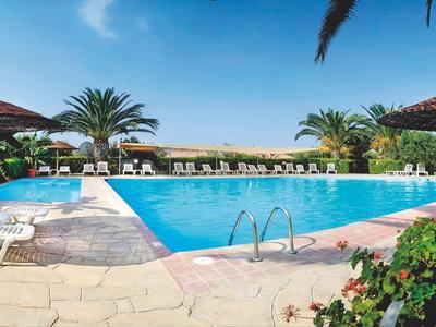 Grande piscina all'aperto con lettini e piante sotto un cielo azzurro.