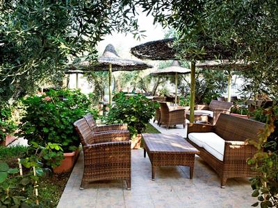 Area salotto accogliente con mobili in rattan attorno a un tavolo, circondata da piante verdi sotto un tetto ombreggiato.