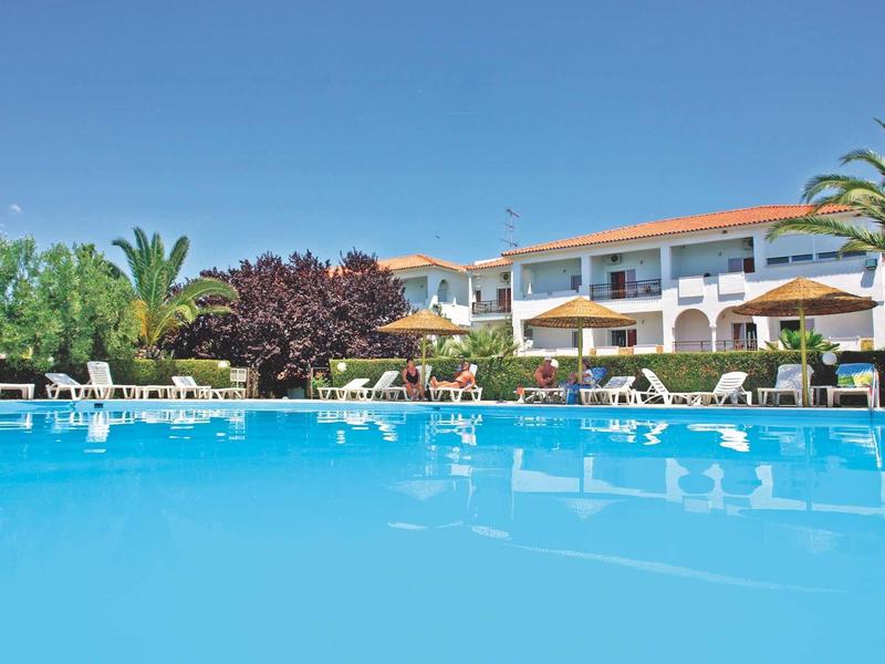 Area piscina con acqua blu chiara, due file di lettini e edificio hotel su più piani sullo sfondo