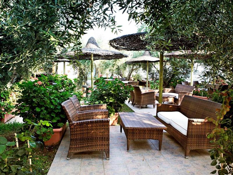 Area salotto accogliente con mobili in rattan attorno a un tavolo, circondata da piante verdi sotto un tetto ombreggiato.