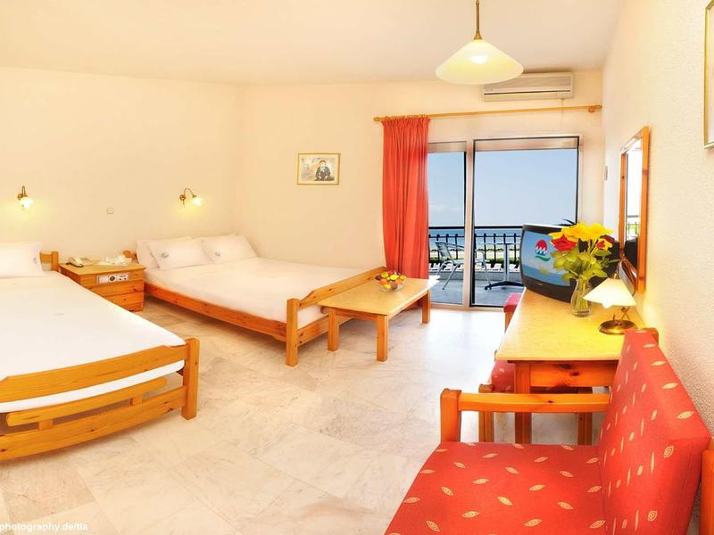 Camera d'hotel luminosa con due letti, balcone e vista mare.