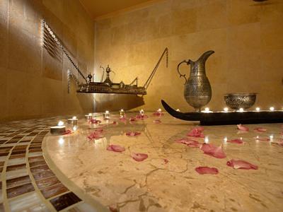 Ein warmer Raum mit Marmorbad, Kerzenlicht und Rosenblättern auf der Badewanne aus Stein.