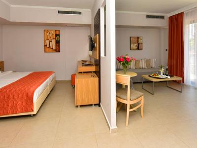 Geräumiges Hotelzimmer mit Doppelbett, Schreibtisch, Sofa, Tisch und Zugang zu Terrasse mit Gartenblick.