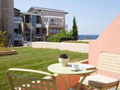 Terrasse mit Rundtisch, Stühlen, Pflanze, Rasen, Häusern und Blick aufs Meer.