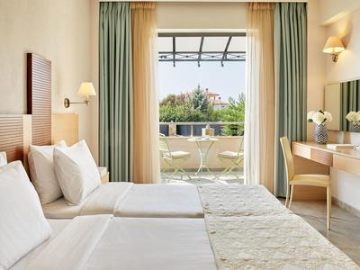 Hell eingerichtetes Hotelzimmer mit zwei Betten, hellen Vorhängen und Balkon mit Blick ins Grüne.