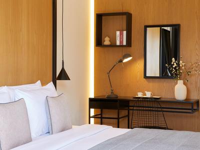 Modernes Schlafzimmer mit hellem Holz, Bett, schwarzem Wandregal, Schreibtisch und Spiegel.