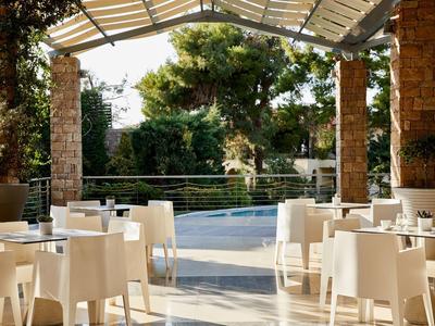 Freiluftcafé mit weißen Tischen und Stühlen unter Pergola, umgeben von Bäumen und Natur.