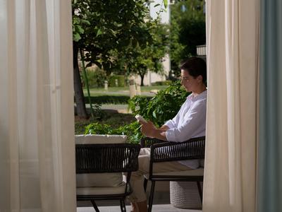 Osoba sedí uvolněně na židli na balkóně s výhledem na zelenou zahradu
