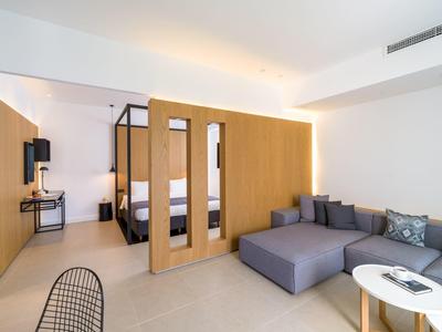 Moderní hotelový salón s šedou pohovkou, dřevěnou stěnou a televizí na zdi.