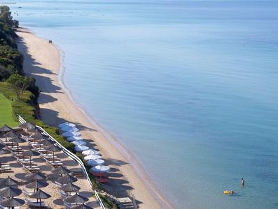 Langer Sandstrand mit Strandliegen und Sonnenschirmen neben klarem, ruhigem Meer.