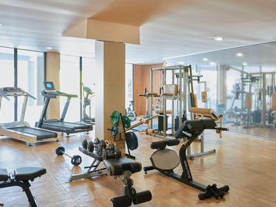 Moderner Fitnessraum mit Fitnessgeräten, Hanteln und großen Fenstern mit Blick auf die Stadt.