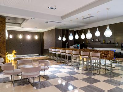 Moderní hotelový bar s bílými kapkovými světly, koženými sedadly a pruhovanou mramorovou podlahou