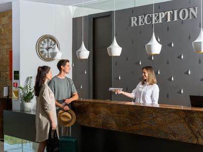 Hotelová recepce s recepční a hosty, moderní recepční pult a osvětlení.