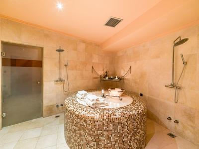 Kruhová mozaiková vířivka v světlé koupelně se sprchou a skleněnou skříňkou.