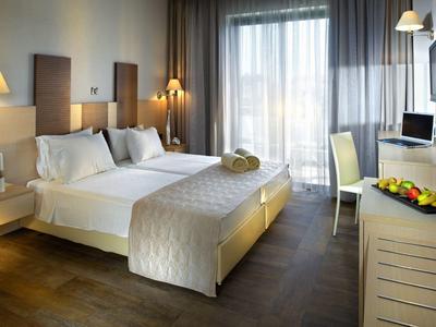 Modernes Hotelzimmer mit Doppelbett, Schreibtisch, Fernseher und großem Fenster mit Vorhängen.