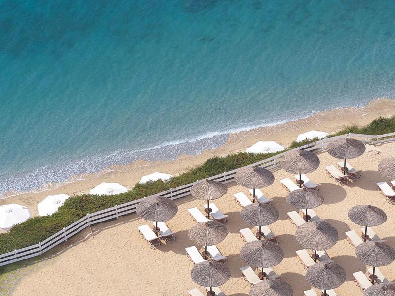 Pláž s řadami slunečníků a čistou modrou vodou u břehu