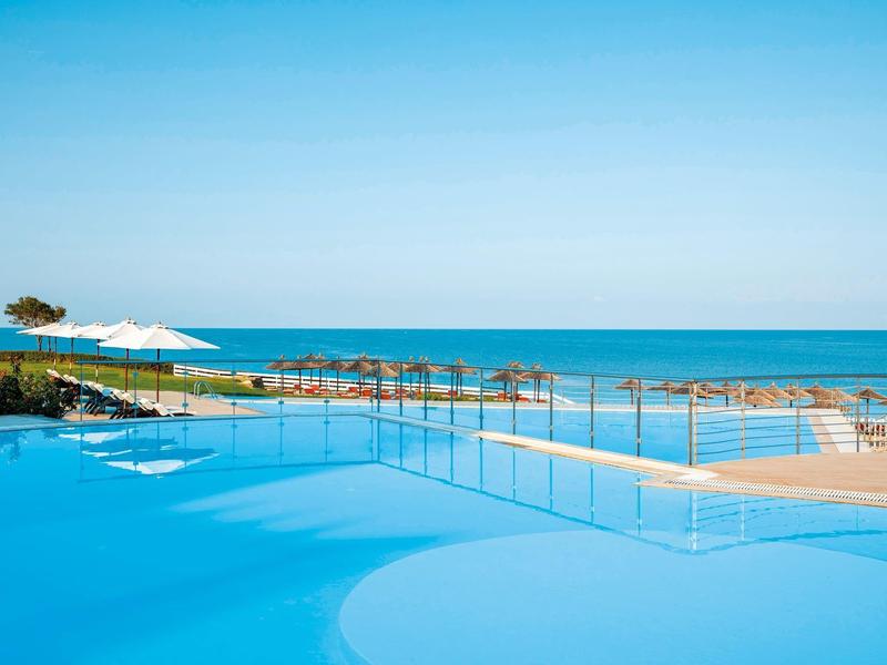 Moderní venkovní bazén s výhledem na moře a lehátky pod modrou oblohou