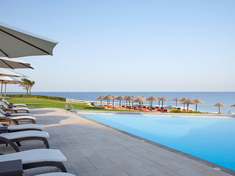 Infinity bazén s lehátky a slunečníky s výhledem na moře za jasné oblohy.