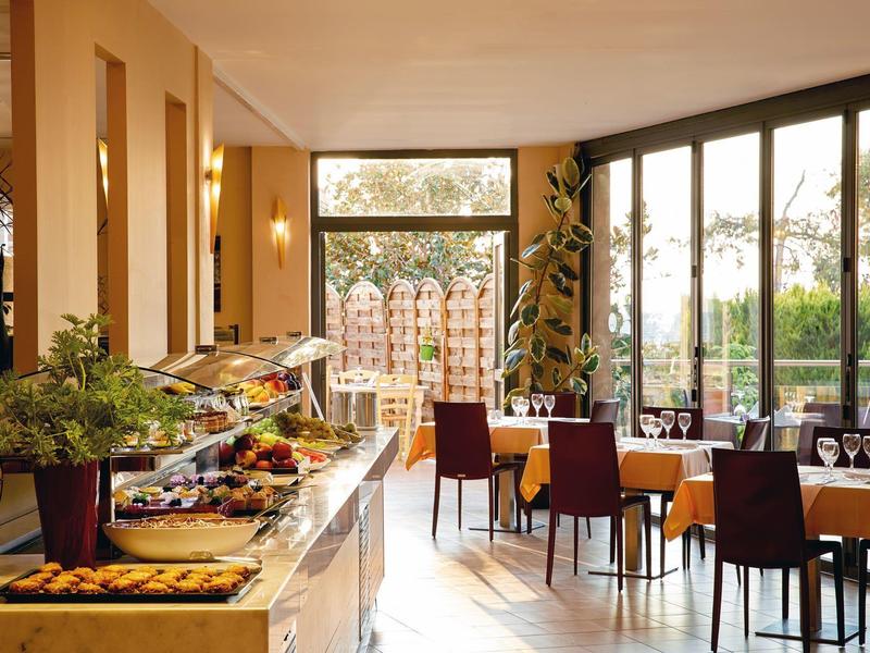 Světla jídelna s velkými okny, prostřenými stoly a bufetovou částí.