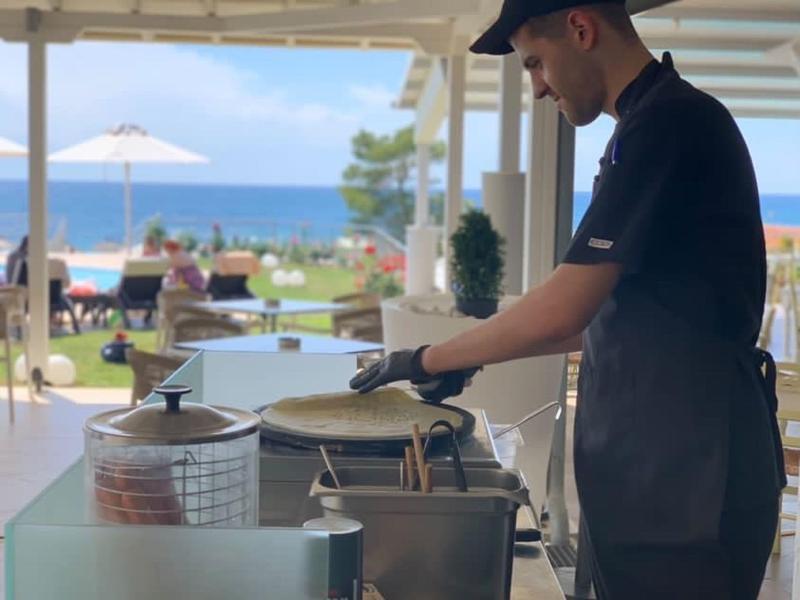 Kuchař připravuje jídlo v otevřené restauraci s výhledem na moře.