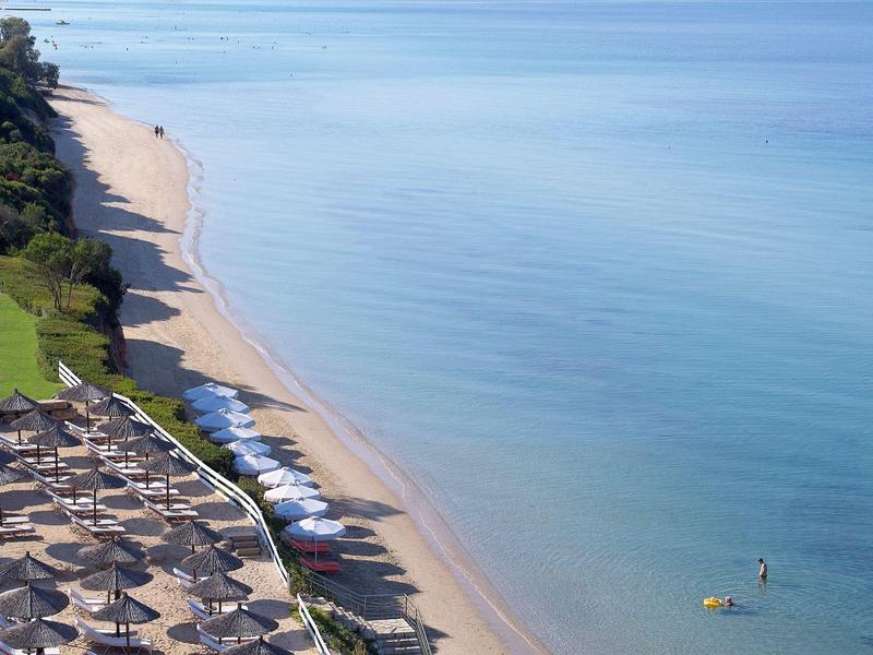 Pláž s pískem, slunečními parasoly a klidnou čistou vodou v slunečný den.