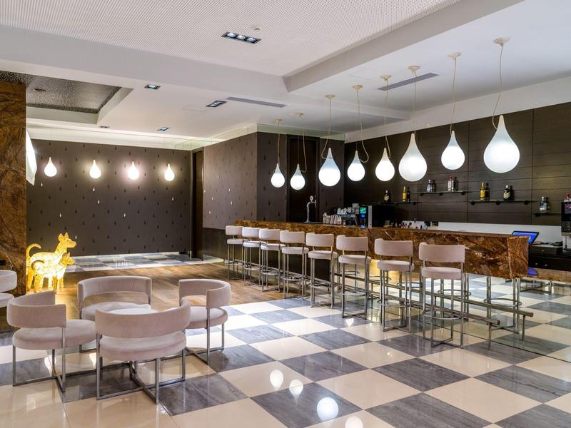 Moderní hotelový bar s bílými kapkovými světly, koženými sedadly a pruhovanou mramorovou podlahou