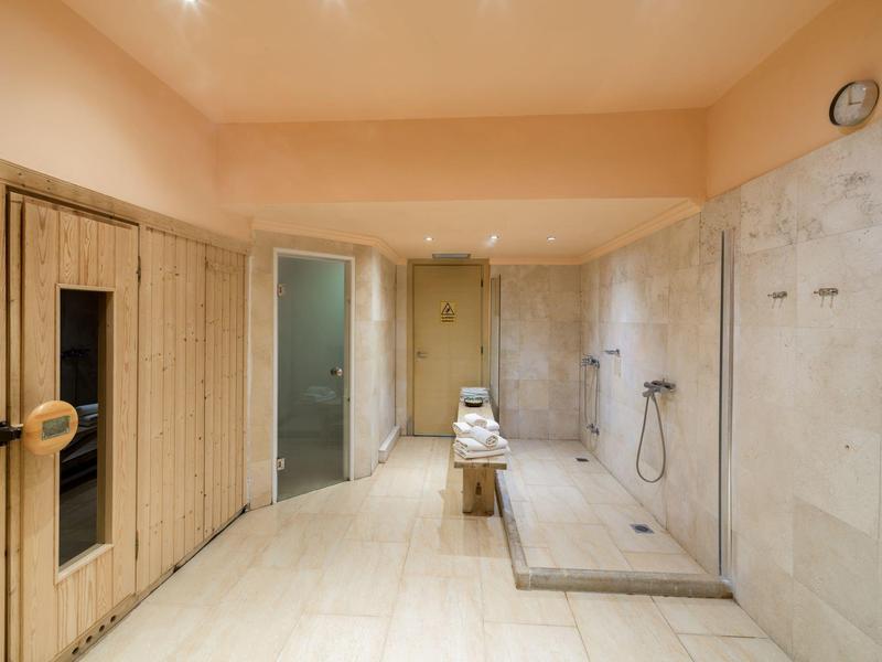 Moderní wellness prostor se saunou a bezbariérovým sprchovým koutem v teplých odstínech.