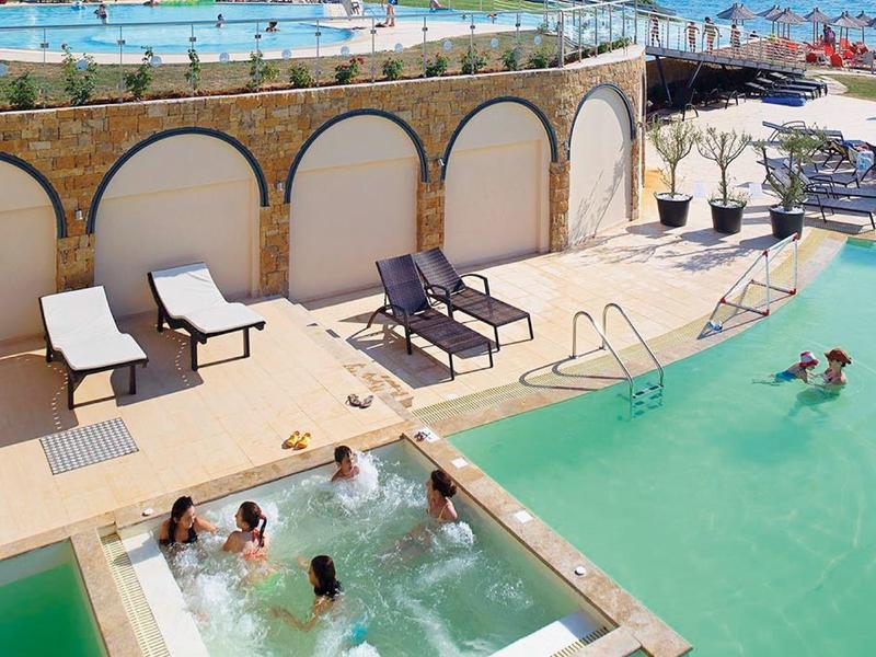 Venkovní bazén s vířivkou a lehátky v slunném plážovém hotelu.