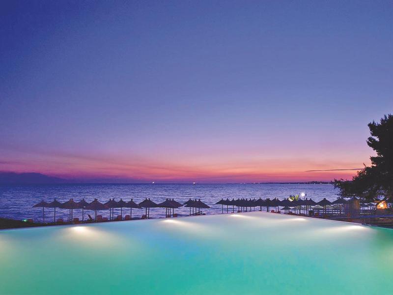 Infinity bazén s osvětlenou vodou a západem slunce nad mořem v pozadí