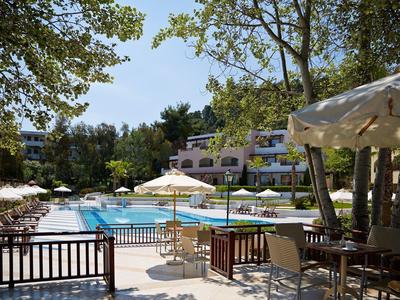 Venkovní bazénová oblast s lehátky a slunečníky v hotelu s stromy v pozadí.