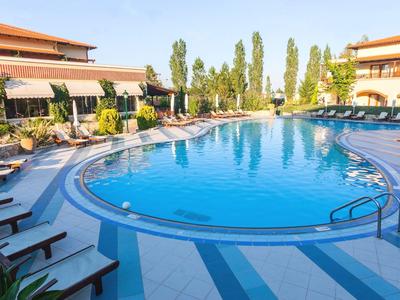 Großer runder Swimmingpool mit Sonnenliegen und Gebäuden bei sonnigem Wetter.