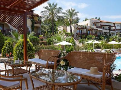 Hotelterrasse mit Korbmöbeln, Glas-Tischen, Blick auf Pool und Palmen bei sonnigem Wetter.