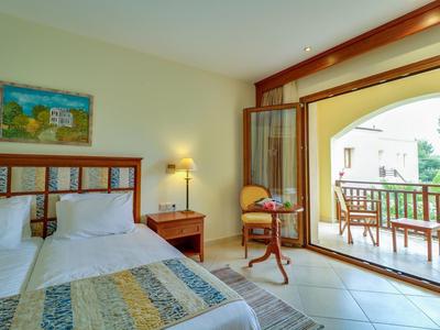 Světý hotelový pokoj s manželskou postelí a otevřeným balkonem se sezením a výhledem.