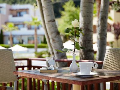 Kaffeetasse und Vase auf Holztisch im Außenbereich eines Hotels mit Pflanzen und Stühlen.