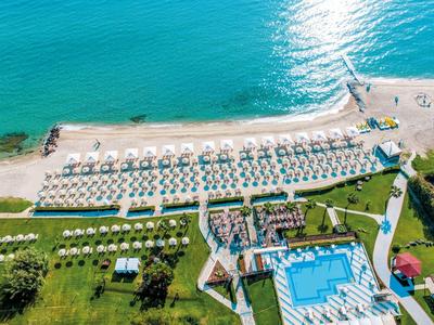 Strand met rijen parasols en ligstoelen naast zwembad en hotelgebouw aan zee.